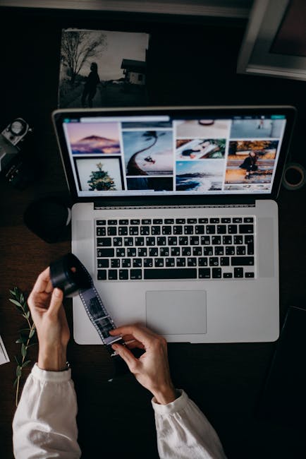 Person handling film strip over laptop with photos, capturing digital and analog photography convergence.